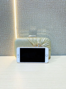 Detailed view of gold evening clutch with rhinestones compared to a smartphone for scale