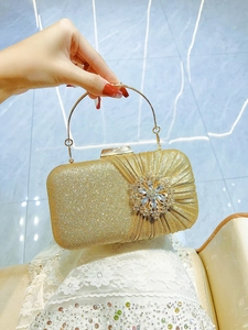Macro detail of gold glitter evening clutch featuring a large 3D rhinestone flower and ring handle