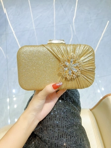 Detailed shot of champagne gold evening clutch featuring 3D crystal flower and pleated design