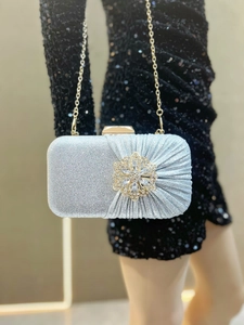 Silver glitter clutch bag with crystal flower detail held by a model in black dress