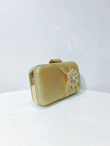 Macro detail of gold glitter clutch bag with pleated texture and sparkling rhinestone flower