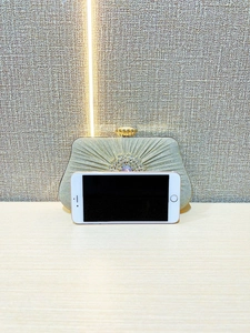 Detail of pleated gold evening clutch bag with crystal floral ornament and metal clasp