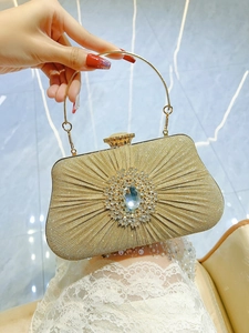 Detail of gold pleated evening clutch featuring a circular rhinestone ornament and ring handle