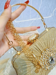 Detailed close-up of a pleated gold evening bag with a crystal flower clasp and metal handle