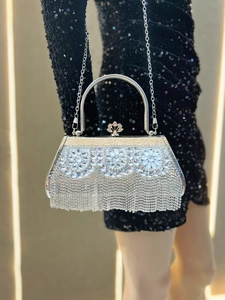 Macro detail of luxury silver evening bag featuring crystal flowers and metallic tassels