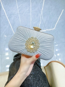 Close-up of pleated silver evening bag with sunflower rhinestone brooch and gold crown clasp