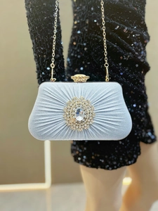 Close-up of pleated satin evening bag with a central rhinestone brooch and gold chain