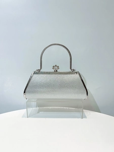 Close-up of silver evening bag with glitter texture and engraved metal handle details
