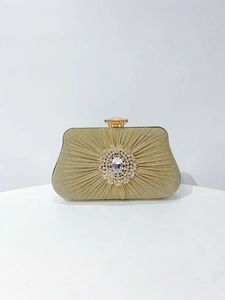 Close-up of pleated gold fabric with a luxury crystal cluster on a formal evening bag