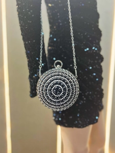 Detail of a spherical black pearl evening bag with rhinestones on a sequin dress