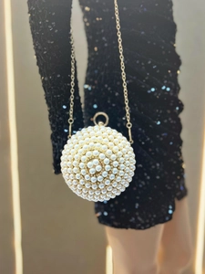 Detailed view of spherical pearl evening bag with gold chain held against a black dress