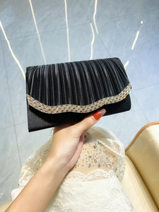 Détail de la pochette de soirée en satin noir plissé avec bordure ondulée en strass