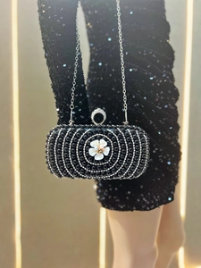 Macro detail of black evening clutch bag with pearls, crystals, and shell flower accent
