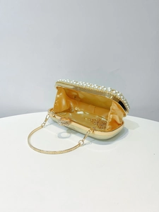 Detail of evening clutch featuring crystal ring clasp and pearl trim in champagne gold