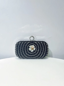 Detailed view of black clutch bag with white floral accent and silver rhinestone circles