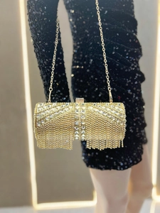 Close-up of luxury gold rhinestone evening bag with elegant tassels on a black gown