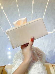 Detailed view of champagne satin bow clutch held with an elegant white lace party dress