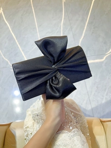 Detail of elegant black satin clutch bag with large bow held against white lace evening dress