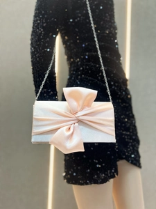 Pink satin evening clutch with large bow detail and silver chain strap on model
