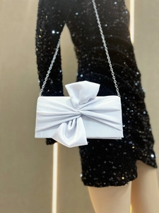 Detail of silver satin clutch featuring a large bow and delicate metal chain strap