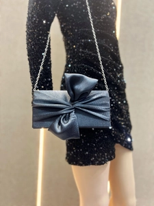 Detail of elegant dark grey bow evening clutch with silver chain on black sequin dress