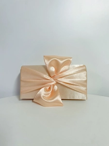 Detail of champagne satin evening clutch featuring a large elegant silk bow decoration