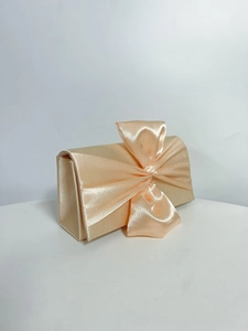 Detail of elegant apricot satin evening clutch featuring a large decorative bow on front