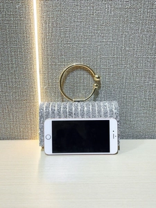 Silver sequin evening clutch with gold metal handle next to a phone for size comparison
