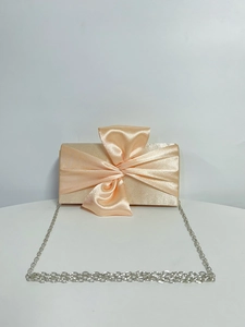 Detail of champagne satin evening clutch featuring a large 3D bow and silver chain strap