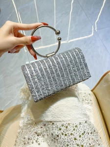 Detail of silver rhinestone evening bag with round metal handle held against lace dress