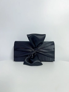Detailed close-up of a black satin evening clutch featuring a large elegant bow decoration