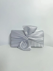 Detail of silver satin evening clutch bag featuring a large decorative bow and pleats