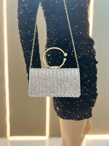 Sparkly silver evening clutch with gold circular handle and chain strap held by a model