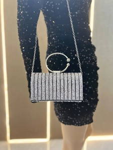 Detail of silver sequined evening clutch with round metal handle and sparkling rhinestone stripes