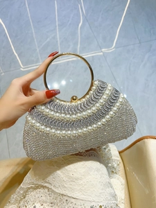 Détail de pochette de soirée luxueuse avec strass argentés, perles et anse en métal doré