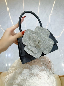 Detailed view of black satin handbag featuring a luxury 3D rhinestone camellia flower design