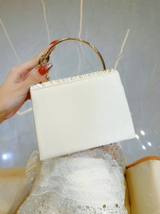 Detail of white satin evening bag with golden ring handle and floral clasp for weddings