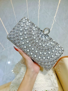 Close-up of silver evening clutch featuring hollow metal lace, pearls and crystal clasp