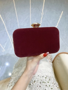 Pochette in velluto bordeaux con chiusura dorata tenuta da una mano in abito di paillettes