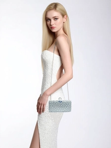 Detail of luxury evening clutch bag with radiating pearls and diamonds on a white dress