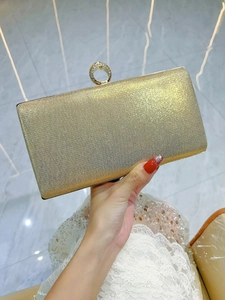 Close-up of champagne gold glitter evening clutch with sparkling rhinestone ring handle
