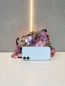 Pink sequin evening bag with gold chain strap shown next to a smartphone for size reference