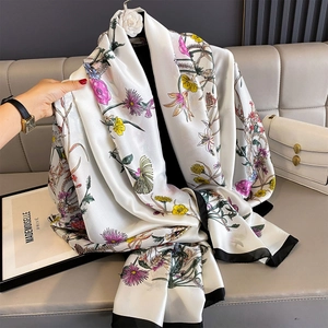 Detailed view of floral silk scarf with elegant black border on a soft sofa