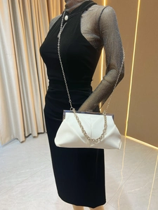 Detailed view of a white cloud clutch bag with silver chain strap on a black evening dress