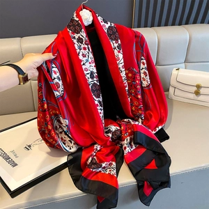 Detail view of red floral silk scarf with black and white borders on a leather sofa
