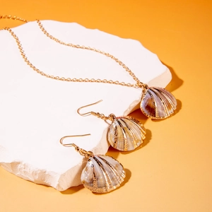 Detail of shell jewelry set with gold necklace and earrings on a white stone pedestal