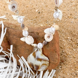 Close-up of Bohemian shell necklace with pearls on natural rock and sand background