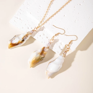 Detail of gold seashell necklace and earrings set on textured stone with warm lighting