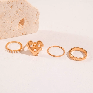 Four-piece gold stacked ring set with heart and faux pearls on a beige sand background