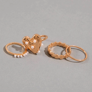 Set of four gold-colored heart and pearl stacking rings for women on light grey background